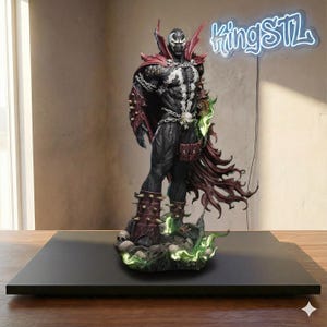 May include: A detailed Spawn action figure, featuring a black and white body with red accents, chains, and a flowing cape. The figure stands on a base with skulls and green glowing effects. The neon sign above reads "kingSTL".