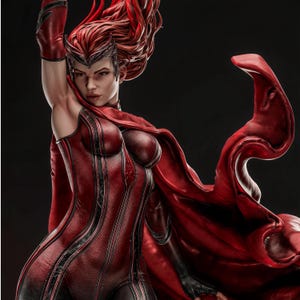 May include: A detailed figurine of a character with long, flowing red hair and a dark red, textured bodysuit. The figure wears a pointed headpiece, matching red gloves, and a long, billowing red cape that extends to the right side of the frame.