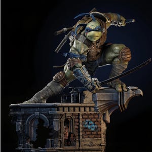 Peut inclure: Une figurine articulée de tortue verte avec un masque bleu, portant une armure en cuir marron et des protège-bras. La figurine tient un sabre katana tout en étant accroupie sur une base architecturale en briques texturées et usées.