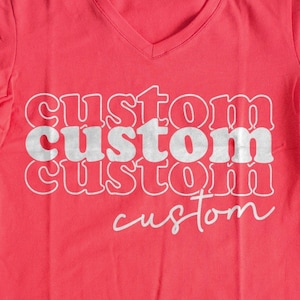 Puede incluir: Una camiseta roja de cuello en V con la palabra "custom" impresa cuatro veces en un diseño apilado y superpuesto. La palabra "custom" está en blanco y tiene un aspecto ligeramente desgastado.
