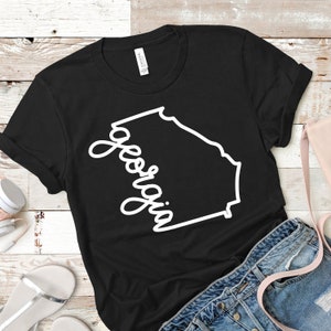 May include: Black t-shirt with a white outline of the state of Georgia and the word "Georgia" written in a cursive font.