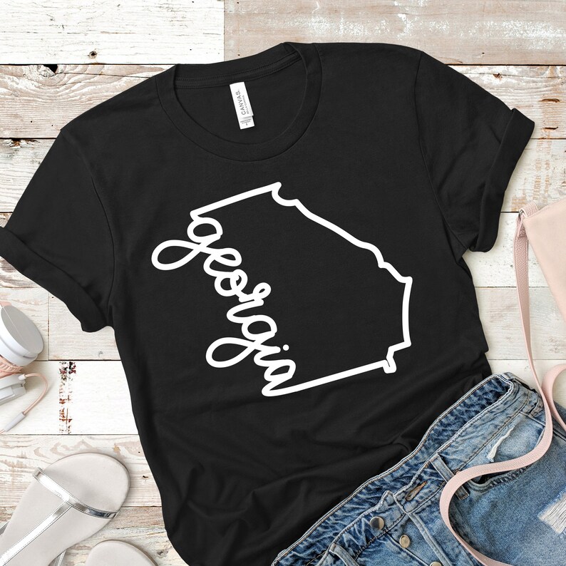 May include: Black t-shirt with a white outline of the state of Georgia and the word "Georgia" written in a cursive font.