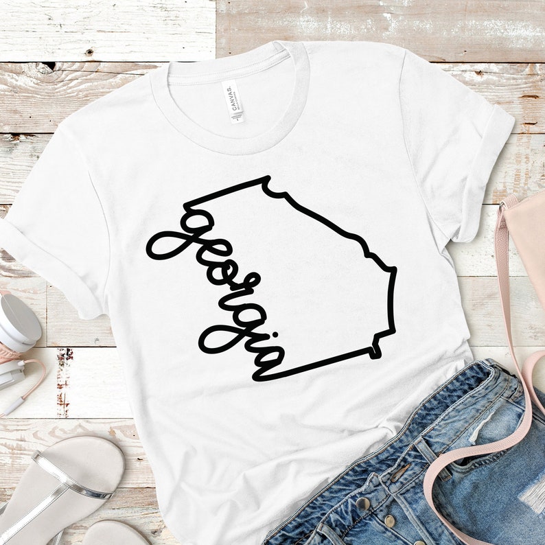 May include: White t-shirt with a black outline of the state of Georgia and the word "Georgia" written in cursive.