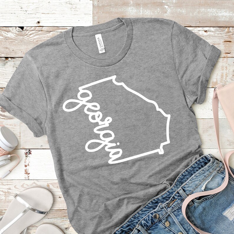 May include: A gray t-shirt with a white outline of the state of Georgia and the word "Georgia" written in a cursive font.