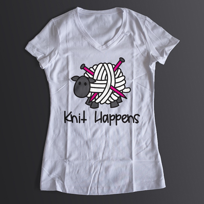 Puede incluir: Camiseta blanca con un gr&aacute;fico de una oveja negra sosteniendo una bola de lana con agujas de tejer rosas. El texto "Knit Happens" est&aacute; impreso debajo de la oveja.