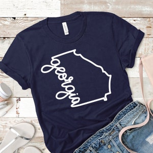 May include: A navy blue t-shirt with a white outline of the state of Georgia and the word "Georgia" written in a cursive font.