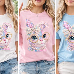 以下が含まれることがあります： 白、ピンク、青の3枚のTシャツ。それぞれに風変わりなウサギのデザインが施されています。ウサギはパッチワーク模様、丸いメガネ、真珠のネックレスをしています。デザインにはリボンと花のアクセントが含まれています。
