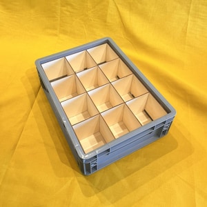 Könnte beinhalten: Eine graue Kunststoff-Aufbewahrungsbox mit einem Gitter aus Holzteilern. Die Box ist rechteckig und hat an jedem Ende einen Griff. Die Teiler schaffen 12 einzelne Fächer.