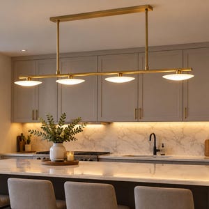 May include: A linear pendant light fixture with a brushed brass finish and four flat, circular, white frosted glass shades. The fixture is suspended by two vertical rods from a rectangular ceiling mount, providing downward illumination.