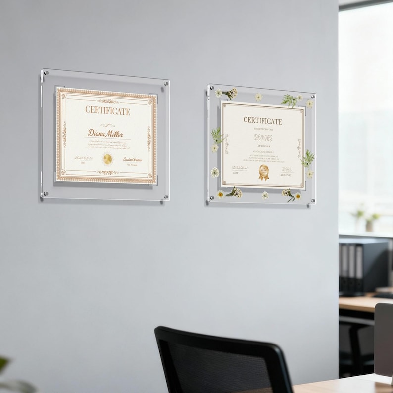 May include: Two clear acrylic certificate frames mounted on a gray wall. Each frame holds a certificate with gold and beige accents. One certificate is plain, the other has floral embellishments.