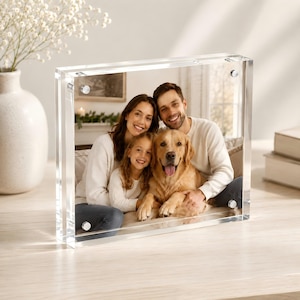May include: A rectangular clear acrylic photo frame featuring four silver magnetic corner fasteners. The frame displays a photograph of a smiling family consisting of two adults, a young child, and a golden retriever dog sitting together.