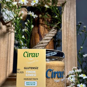 Puede incluir: Un tarro de pasta de avellanas con una etiqueta que dice "Cirav 1940" y "Sin gluten". El tarro se muestra con una caja de la misma marca y rodeado de flores blancas. El tarro contiene 270 gramos de pasta de avellanas.