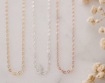 May include: Four delicate chain necklaces in silver, gold, and rose gold. The necklaces are displayed on a white marble surface with dried flowers.