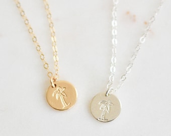 May include: Two delicate necklaces with palm tree pendants. One necklace is gold and the other is silver.