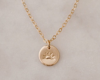 May include: A gold chain necklace with a small, round pendant featuring a sun design.