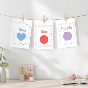 May include: Three cards with the colors blue, red, and purple are displayed. Each card has a white background with a decorative border and a shape or object in the corresponding color. The cards are hanging from a string with wooden clothespins.