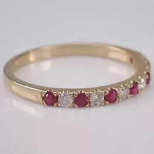 Könnte beinhalten: Ein Goldring mit einer abwechselnden Reihe aus runden roten Rubinen und klaren weißen Diamanten, die in der vorderen Hälfte der Ringschiene gefasst sind. Das Metall hat eine polierte Oberfläche und die Steine bilden ein wiederkehrendes Muster.