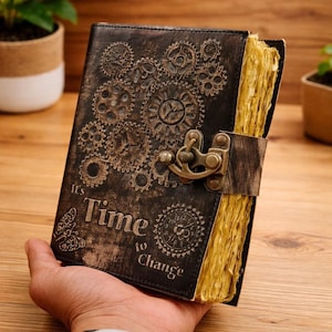 May include: A steampunk-style journal with a dark brown leather cover embossed with gears and the words "It's Time to Change." The journal has a metal clasp and aged, yellowed pages. A butterfly and clock design are also visible.