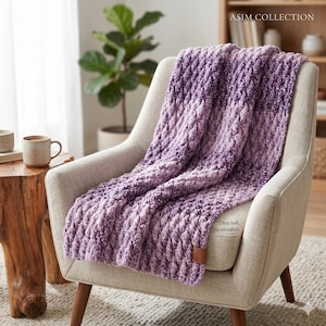 May include: A chunky knit throw blanket in an ombre purple color palette, featuring a textured, raised stitch pattern. The blanket includes a small brown leather-like tag with the text ASIM and the printed text Ultra Soft, Handcrafted.