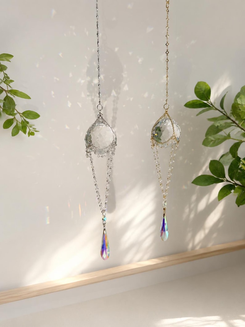 Puede incluir: Dos atrapasoles de cristal colgantes. Uno tiene una cadena plateada y el otro una cadena dorada. Cada uno presenta una bola de cristal transparente y un prisma en forma de l&aacute;grima que refracta la luz en un arco&iacute;ris de colores. Decorativo.