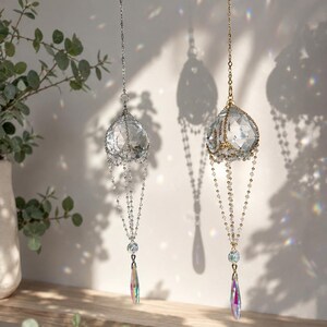 Puede incluir: Dos atrapasoles de cristal colgantes. Uno tiene una cadena plateada y el otro una cadena dorada. Cada atrapasol tiene un orbe de cristal facetado y un prisma en forma de l&aacute;grima. Los prismas reflejan la luz, creando arco&iacute;ris.