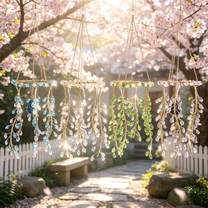 Puede incluir: Cuatro adornos colgantes decorativos con marcos y cadenas doradas. Cada adorno presenta un anillo adornado con cristales y acentos colgantes en forma de cristal y hoja en azul, transparente y verde. Los adornos cuelgan frente a una valla blanca y un camino de piedra.