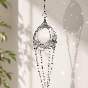 Puede incluir: Un atrapasoles de cristal transparente con un cristal principal facetado en forma de l&aacute;grima. Cuelga de una cadena plateada y presenta hebras de peque&ntilde;as cuentas transparentes. El atrapasoles est&aacute; dise&ntilde;ado para atrapar y reflejar la luz.