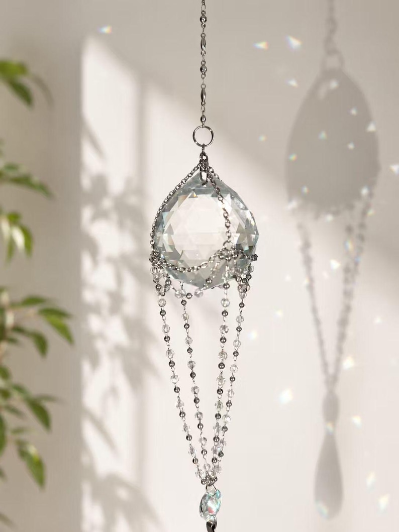 Puede incluir: Un atrapasoles de cristal transparente con un cristal principal facetado en forma de l&aacute;grima. Cuelga de una cadena plateada y presenta hebras de peque&ntilde;as cuentas transparentes. El atrapasoles est&aacute; dise&ntilde;ado para atrapar y reflejar la luz.