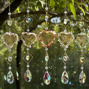 Peut inclure: Une collection de capteurs solaires suspendus avec des accents en forme de cœur et de losange. Chaque capteur solaire présente un motif de papillon doré à l'intérieur d'un cœur, entouré de cristaux colorés et de pendentifs en forme de goutte. Les capteurs solaires sont suspendus à de fines chaînes.