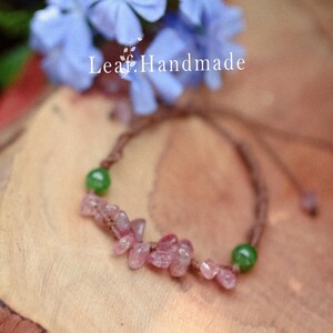 May include: A handmade bracelet featuring pink gemstone chips and green beads strung on a brown cord. The bracelet is accented with a cluster of pink stones and green beads. The text "Leaf Handmade" is visible in the background.