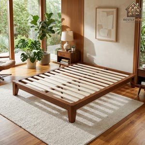 May include: A low-profile wooden bed frame with a natural finish, featuring a slatted base design. The frame is constructed from dark wood and sits directly on the floor, providing a sturdy foundation for a mattress in a bedroom setting.