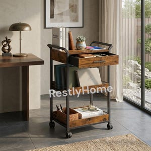 May include: A rolling storage cart with a dark metal frame and rustic brown wood-grain shelves. It features a top drawer, two open lower shelves, and four caster wheels. The cart holds books, a small potted succulent, and office supplies.