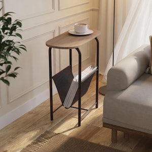 May include: A small, wooden side table with a black metal frame. The table has a rounded top and a built-in magazine rack. A white coffee cup and saucer sit on the table. The table is next to a sofa and a floor lamp. The table is approximately 60 cm tall.