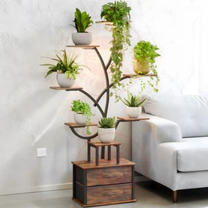 May include: A tall, dark metal plant stand shaped like a tree with multiple wooden shelves holding various potted green plants. The base features a rectangular wooden cabinet with two drawers and metal handles, providing storage space for items.