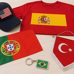 May include: A collection of patriotic items, including a navy blue baseball cap with an American flag patch, a red t-shirt with a Spanish flag design, and a small Brazilian flag keychain.