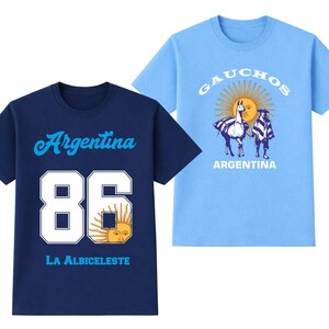 May include: Two short-sleeved t-shirts. One is navy blue with "Argentina" and "86" in white, plus a sun graphic. The other is light blue with "GAUCHOS" and a sun graphic, with two figures and a llama. "ARGENTINA" is printed below.