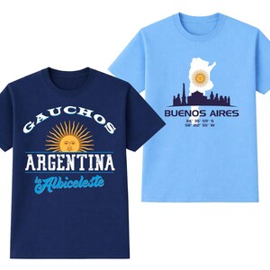 May include: Two short-sleeved t-shirts. One is navy blue with "GAUCHOS ARGENTINA" text and a sun graphic. The other is light blue with a Buenos Aires skyline graphic and coordinates. Both shirts are crew neck.