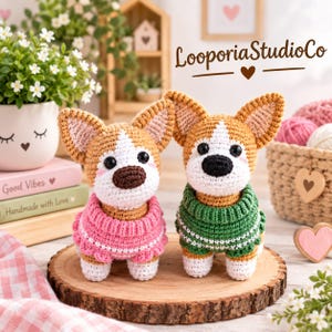 Puede incluir: Dos peluches de corgi tejidos a ganchillo sobre una rodaja de madera. El corgi de la izquierda lleva un suéter rosa y el de la derecha uno verde con detalles blancos. Ambos tienen cuerpos de lana marrón y blanca, ojos y nariz negros. Texto: LooporiaStudioCo.