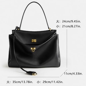 Pu&ograve; includere: Una borsa a mano in pelle nera con manico superiore e tracolla staccabile. La borsa ha finiture dorate e una forma rettangolare. Dimensioni: 35 cm di larghezza, 29 cm di lunghezza e 11 cm di profondit&agrave;. Il manico superiore &egrave; alto 24 cm e la borsa &egrave; alta 21 cm.