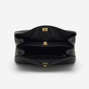 Pu&ograve; includere: Borsa a mano in pelle nera aperta, che rivela i compartimenti interni. La borsa presenta chiusure e dettagli in metallo dorato. Il design &egrave; strutturato, con chiusura a patta e pi&ugrave; sezioni. L'interno &egrave; nero.
