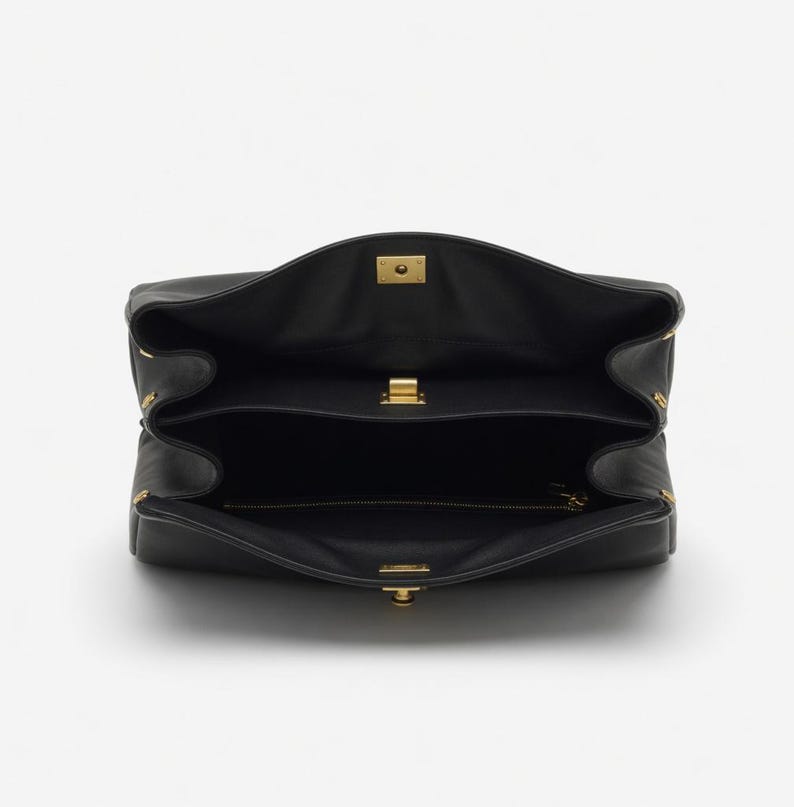 Pu&ograve; includere: Borsa a mano in pelle nera aperta, che rivela i compartimenti interni. La borsa presenta chiusure e dettagli in metallo dorato. Il design &egrave; strutturato, con chiusura a patta e pi&ugrave; sezioni. L'interno &egrave; nero.