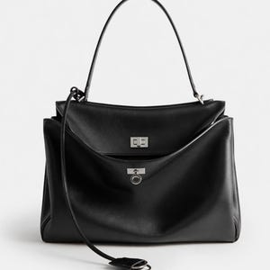Pu&ograve; includere: Borsa a mano in pelle nera con manico superiore e tracolla staccabile. La borsa presenta una chiusura con patta con chiusura argentata e una tasca frontale con dettaglio ad anello argentato. Design strutturato.