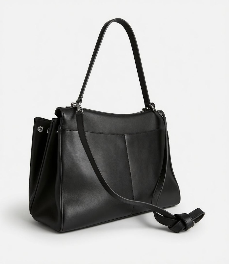 Pu&ograve; includere: Una borsa in pelle nera con tracolla e manico superiore. La borsa ha una forma rettangolare con una tasca frontale e un dettaglio annodato sul cinturino. La borsa &egrave; realizzata in pelle liscia e ha un design minimalista.