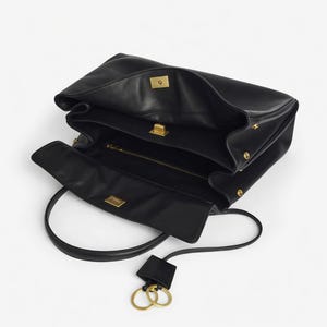 Pu&ograve; includere: Borsa in pelle nera dal design strutturato. La borsa presenta un manico superiore, una tracolla staccabile e finiture dorate. L'interno &egrave; visibile, rivelando pi&ugrave; scomparti e una tasca con cerniera. Un portachiavi con due anelli dorati pende dalla borsa.