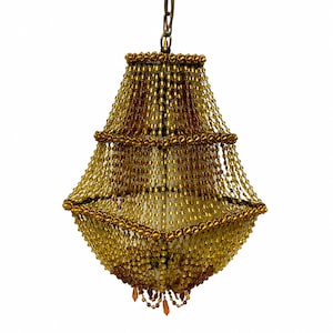 Puede incluir: Una lámpara de araña de varios niveles con numerosos hilos de cuentas de color ámbar y dorado suspendidos de un marco central. La lámpara está sujeta a una cadena de metal en la parte superior, con las cuentas dispuestas en una silueta de cascada en forma de campana.