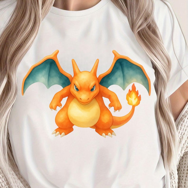 K&ouml;nnte beinhalten: Wei&szlig;es T-Shirt mit einer lebendigen Illustration von Glurak, einem beliebten Pok&eacute;mon vom Typ Feuer und Drache. Das Kunstwerk zeigt Glurak in Orange-, Gelb- und Blaut&ouml;nen mit einem feurigen Schwanz. Das Design ist auf dem Shirt zentriert.