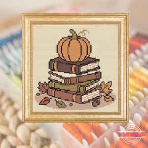 May include: A cross-stitch pattern featuring a stack of four books topped with a single orange pumpkin. The design includes scattered autumn leaves and acorns in shades of brown, green, and orange, all enclosed within a gold-toned frame.