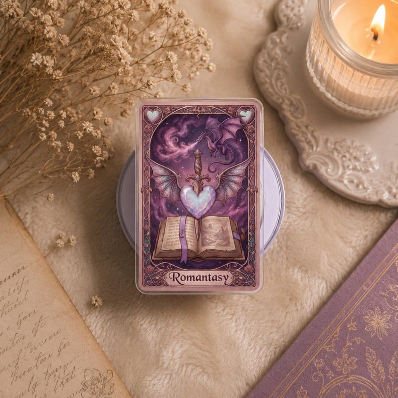 May include: A fantasy-themed card with a purple and pink design. The card features a heart-shaped gem, a sword, and a dragon. The word "Romantasy" is printed at the bottom. The card is on a white surface.