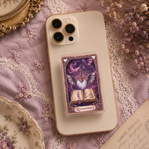 May include: A phone with a pop-up grip featuring a fantasy illustration. The artwork includes a heart pierced by a sword, wings, a dragon, and an open book. The word "Romantasy" is printed at the bottom.