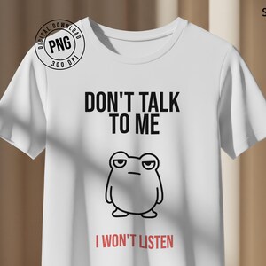 May include: White t-shirt featuring the text "DON'T TALK TO ME" in black, and "I WON'T LISTEN" in red. A cartoon frog with a grumpy expression is below the text. A digital download logo is in the upper left corner.